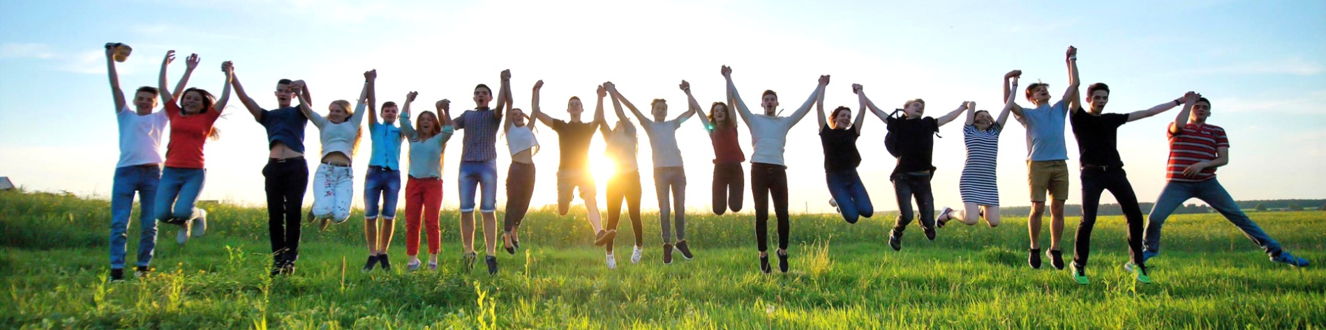 Group of people holding hands and jumping in a grass field